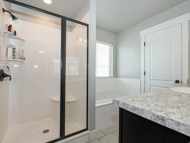 Spacious bathroom featuring a glass-enclosed shower with a built-in seat and integrated shelving, a separate bathtub with a window, dark cabinetry, and a light-toned countertop