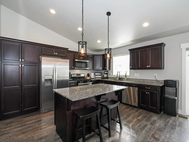Kitchen featuring dark wood cabinetry, stainless steel appliances, granite countertops, and wood-finish flooring