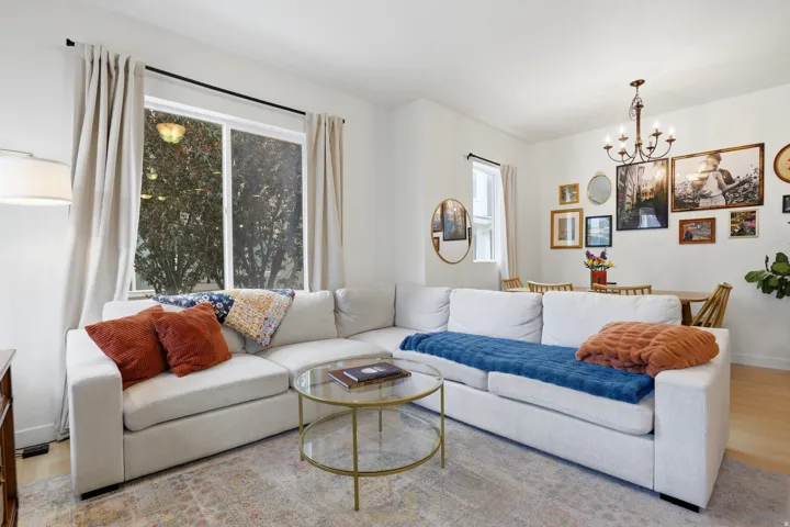 Open-concept living area featuring light wood-finish flooring, a contemporary chandelier, recessed lighting, and a large window with natural light