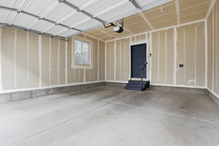 Spacious garage with a concrete floor, overhead garage door, and a dedicated entry door with steps and handrail