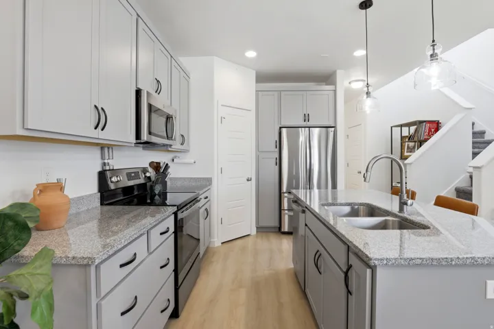 Open-concept kitchen featuring an island with a double basin sink, light wood-finish flooring, light gray cabinetry, stainless steel appliances, and granite countertops