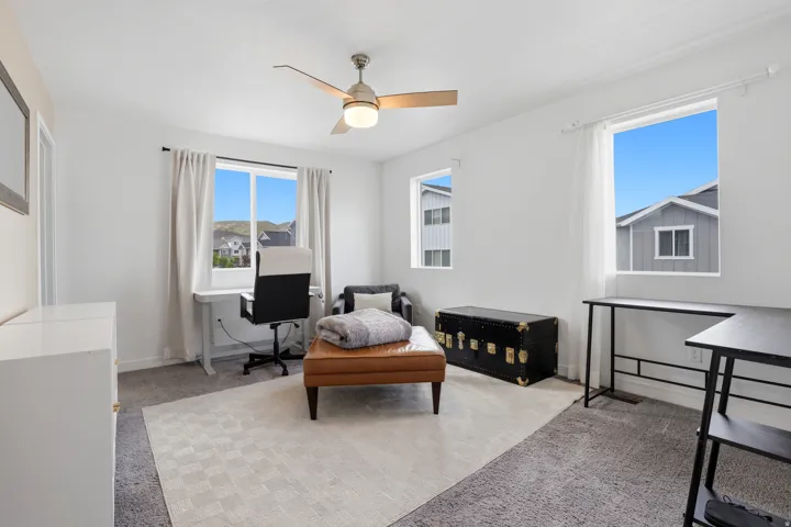 Bright room featuring a ceiling fan with light, multiple windows, and light gray wall-to-wall carpeting