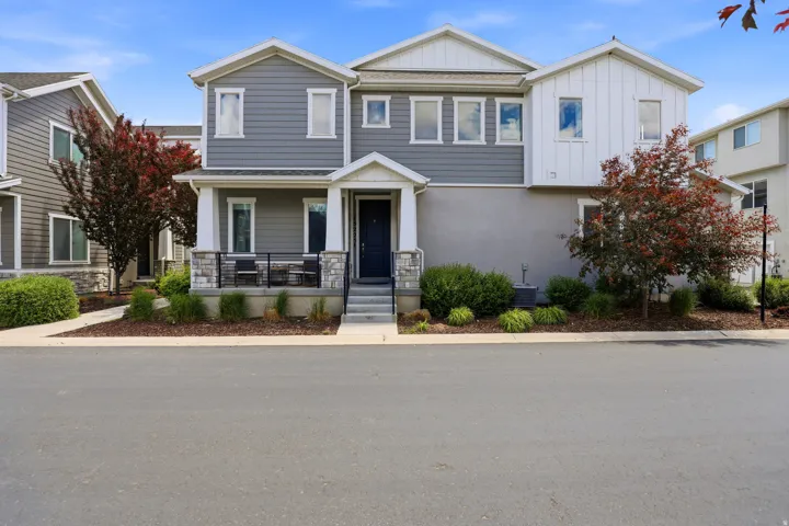 Contemporary multi-story exterior featuring gray siding with white trim, a covered front porch, stone column accents, a dark entry door, and manicured landscaping