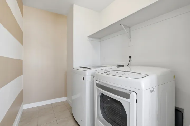 Large dedicated laundry area featuring tile flooring, white baseboards, and a built-in overhead shelf