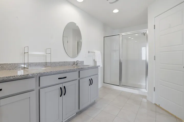 Bathroom featuring a dual vanity with light gray cabinetry and speckled countertops, a glass-enclosed shower, an oval mirror, and recessed lighting
