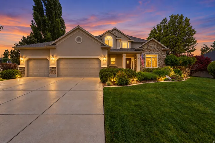 Stucco exterior with stone accents, two-car garage, concrete driveway, front yard landscaping, and exterior lighting