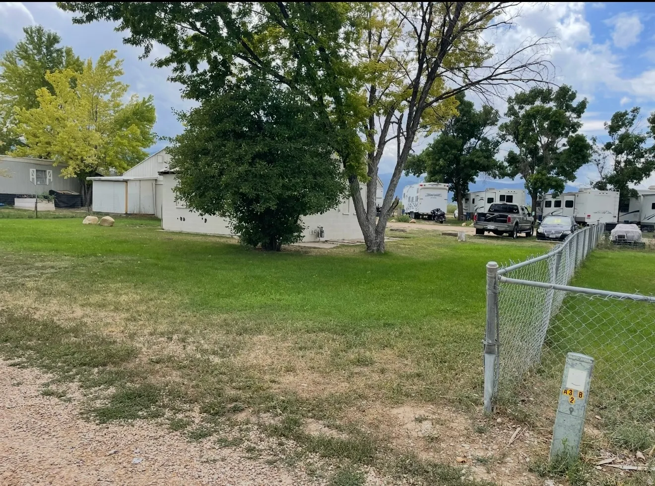 Expansive outdoor space featuring a partial chain link fence, mature trees, and a gravel perimeter