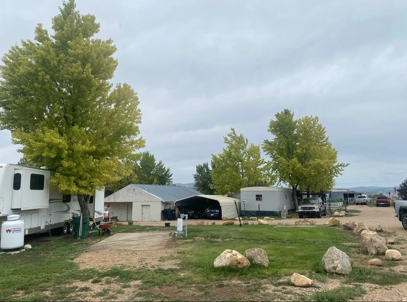 Expansive outdoor property featuring mature trees, a gravel driveway, and a large metal-roofed outbuilding with an attached carport