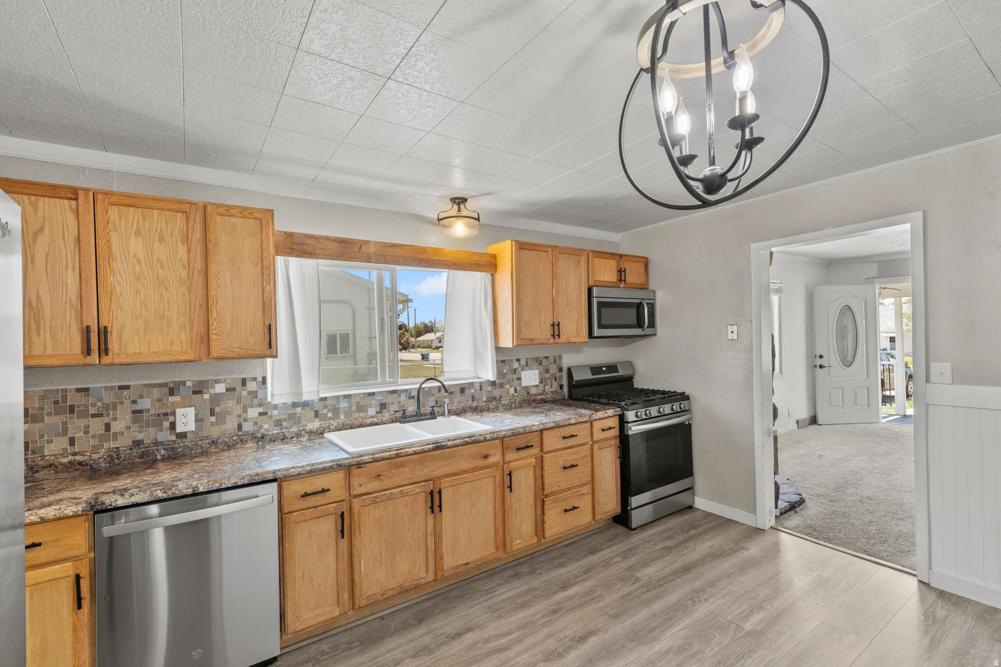 Kitchen featuring wood cabinetry, stainless steel appliances, mosaic tile backsplash, and wood-finish flooring LVP