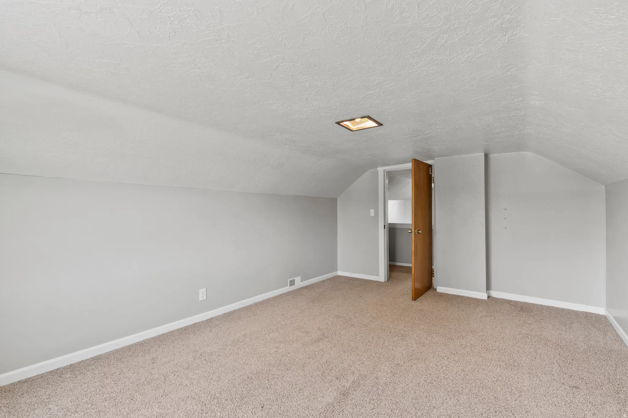 Carpeted room featuring an angled ceiling and light gray walls as a big, 3rd bedroom or another office/family room.