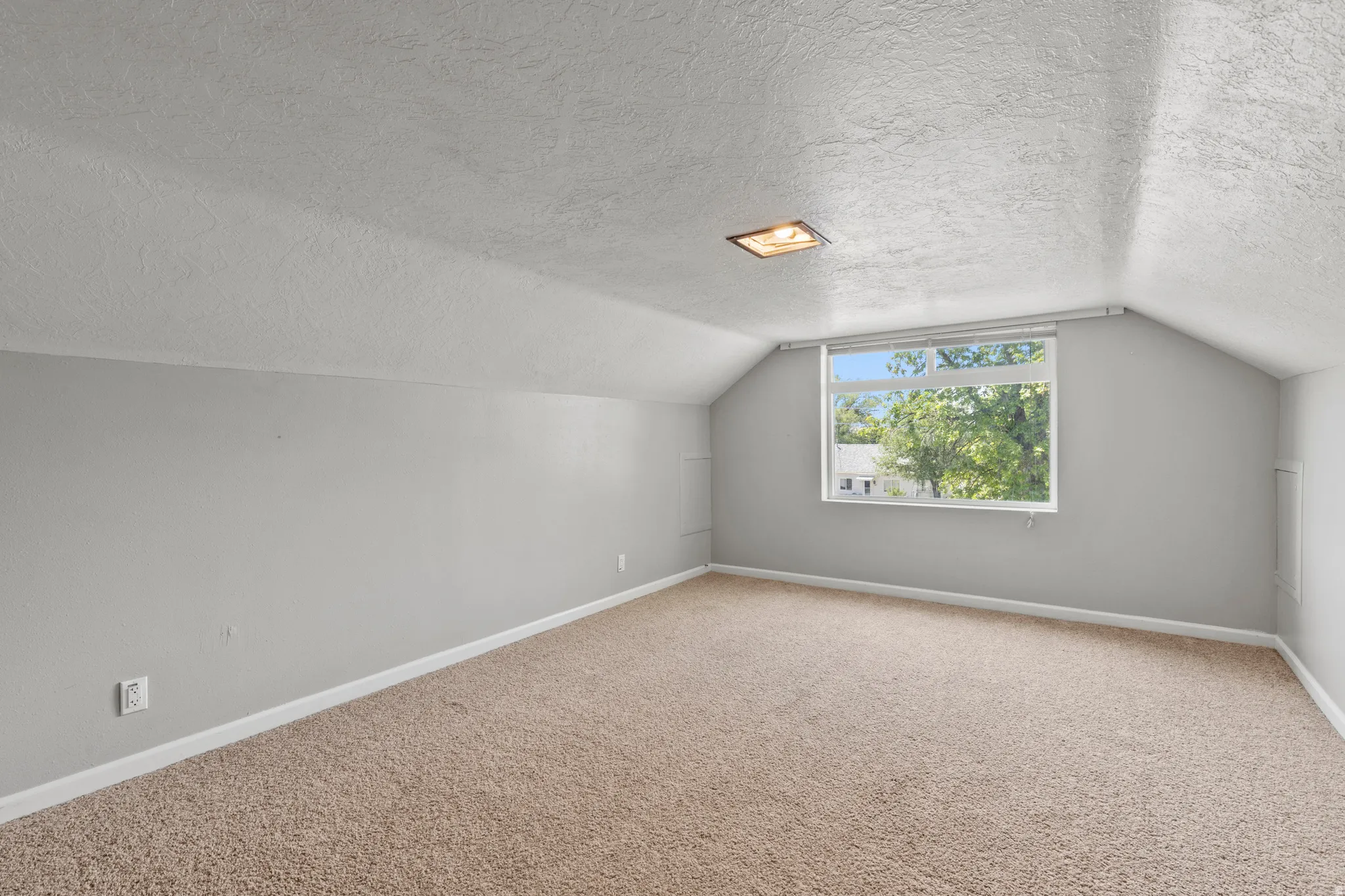 Has been used as the primary bedroom. Carpeted room featuring sloped ceilings, a rectangular window with white trim, and light gray walls. New window.