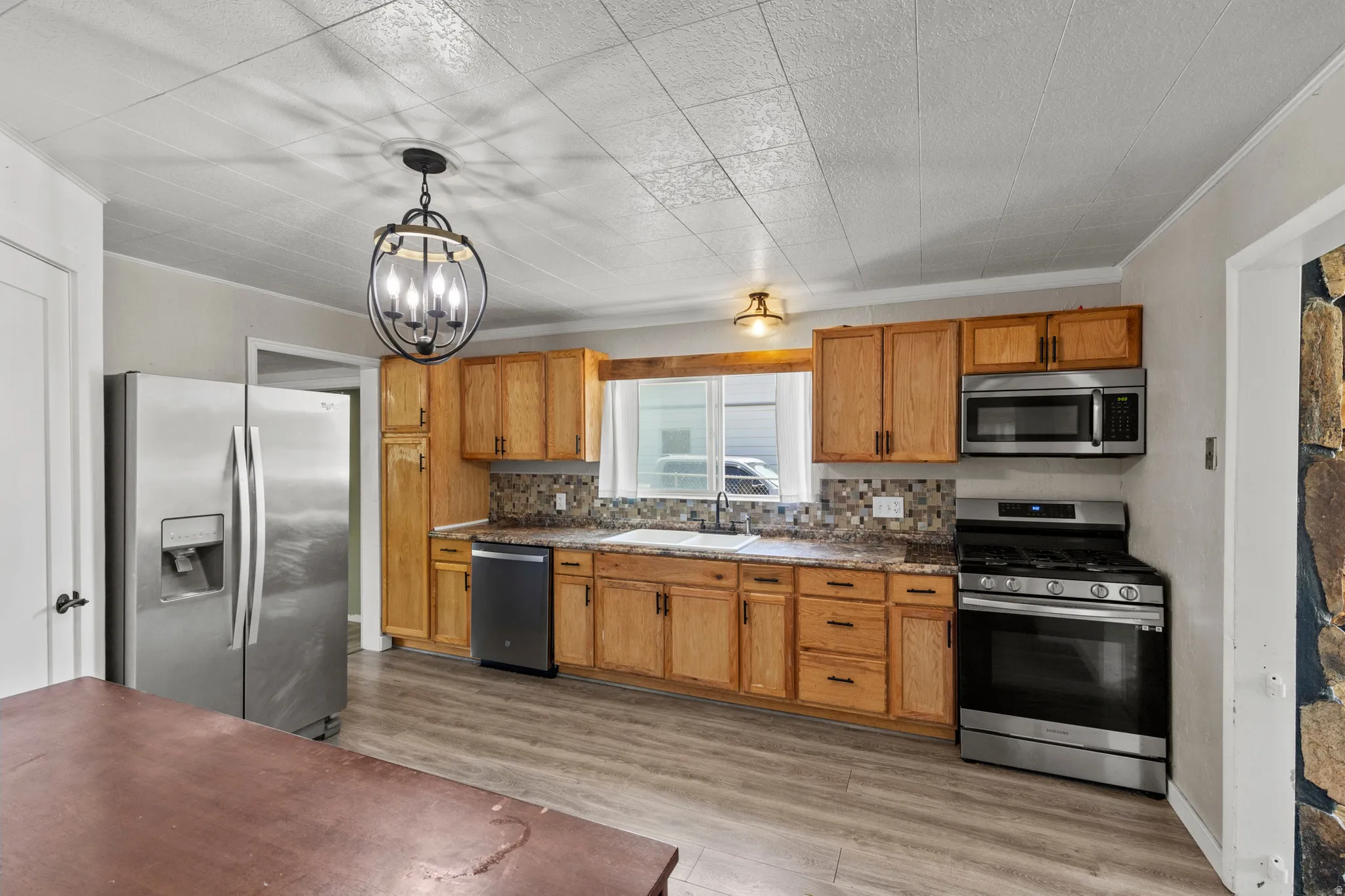 Kitchen featuring LVP wood-finish flooring, wood cabinetry, granite-style formica countertops, mosaic tile backsplash, and stainless steel appliances: Gas oven/range, microwave, refrigerator and dishwasher.
