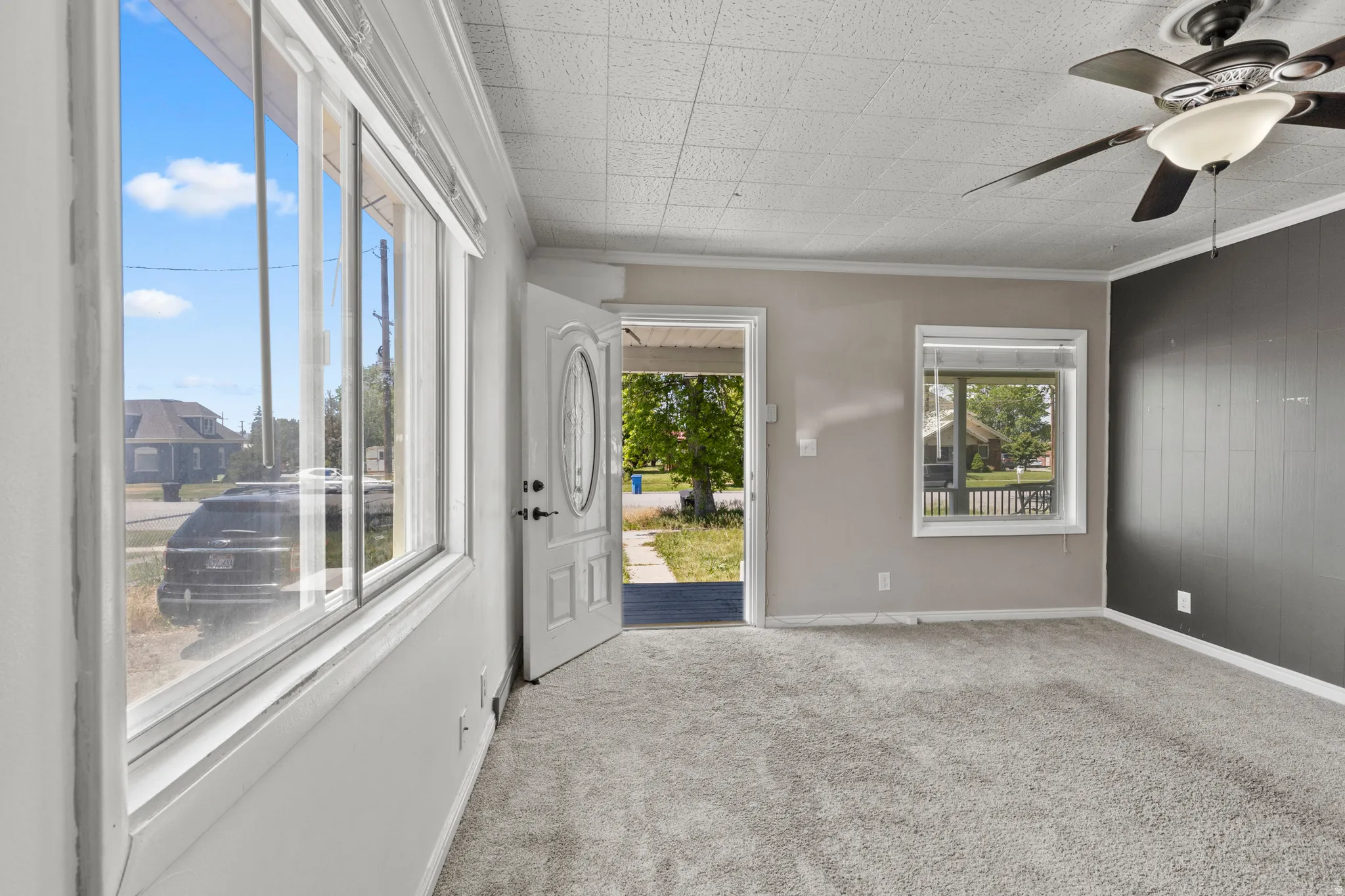 Carpeted interior space featuring a ceiling fan with light fixture, multiple windows, and a paneled accent wall