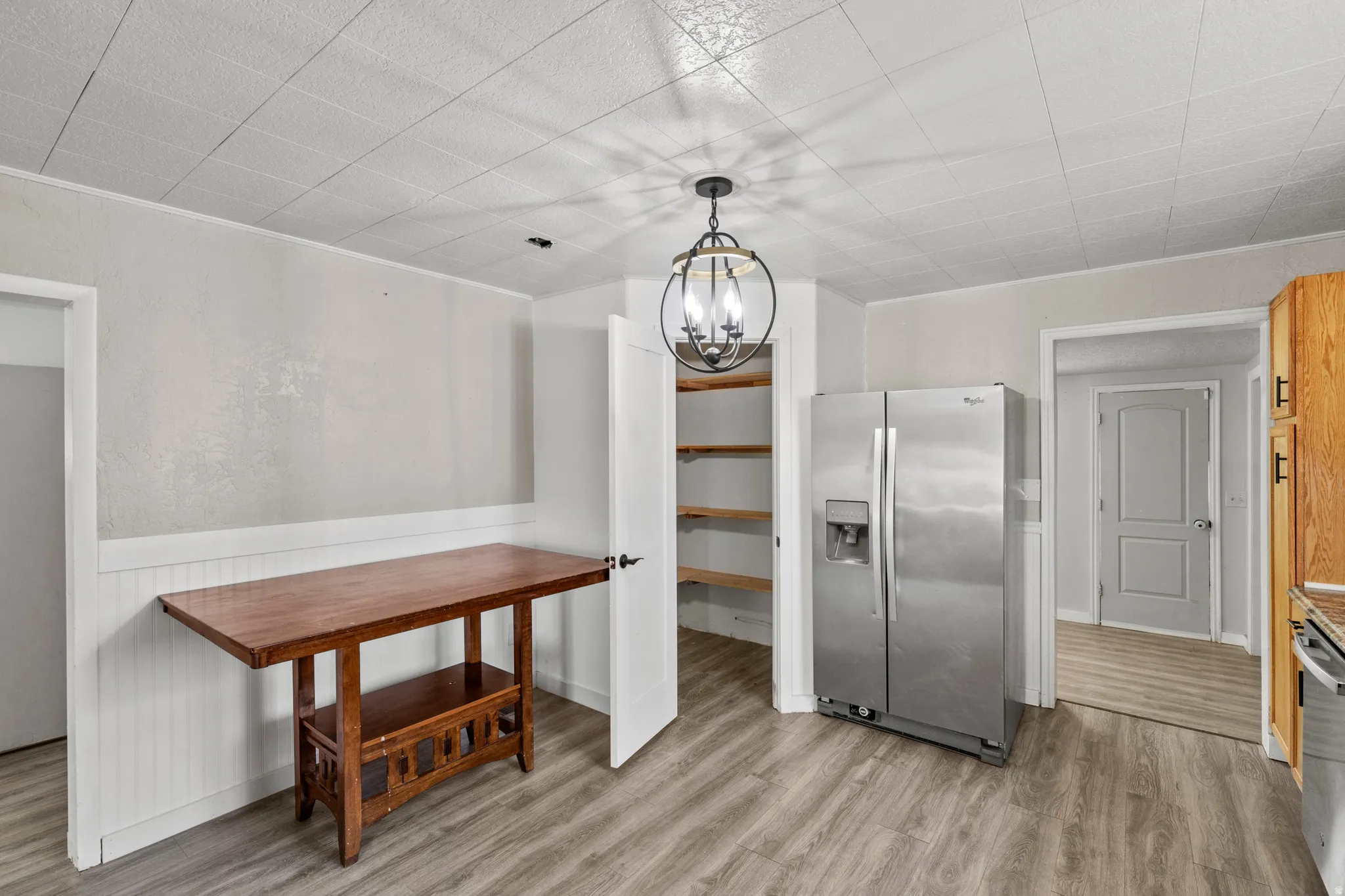 Kitchen area featuring stainless steel refrigerator, wood-finish flooring, white beadboard wainscoting, and a walk-in pantry with built-in shelving