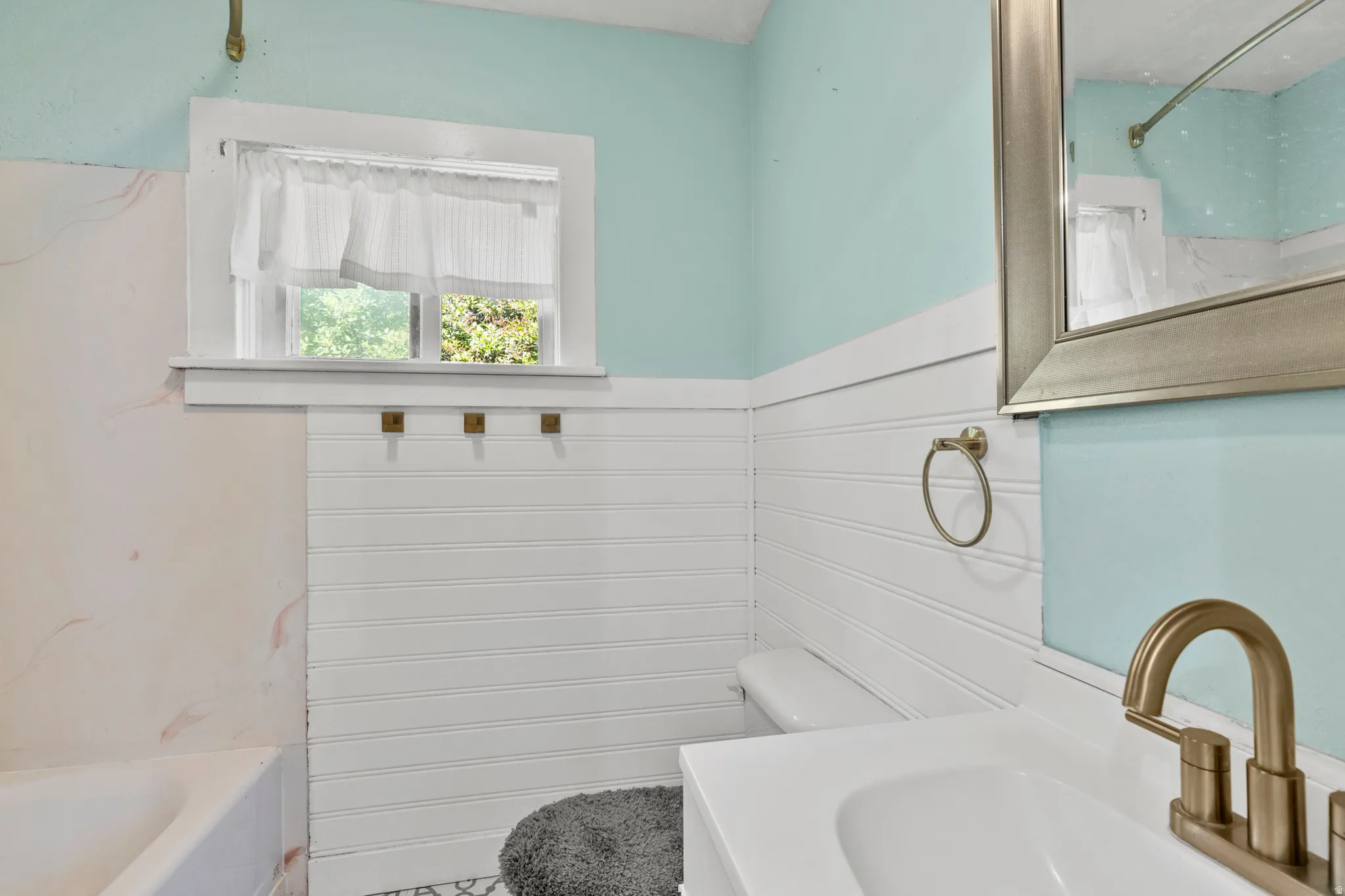 Full Bathroom featuring a white vanity with an integrated sink, brushed gold-tone faucet, and an ornate framed mirror