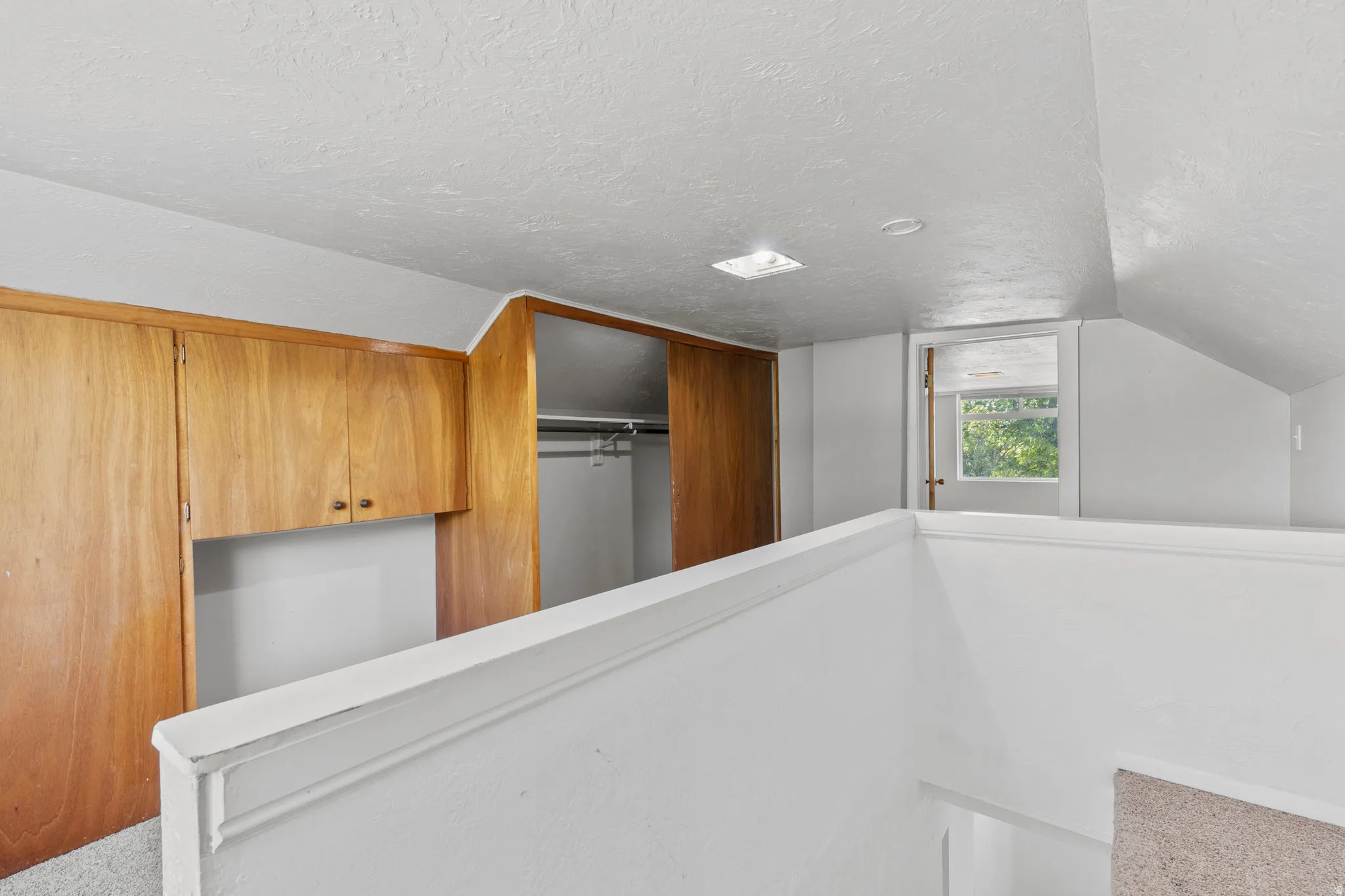 Upper-level landing with built-in wood cabinetry, an open closet with a hanging rod, a window with natural light, and sloped ceilings. Space for two desks or work station.  Great use of space for a multitude of options.