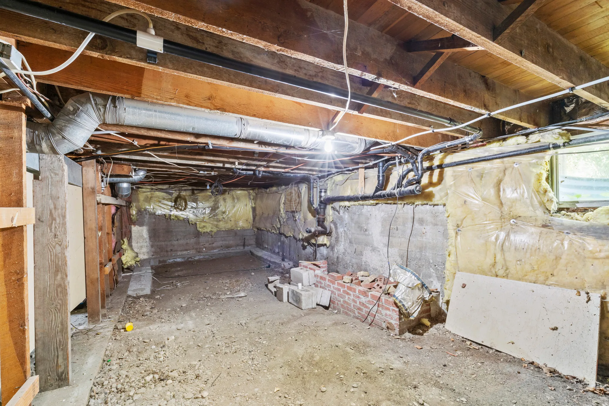 Unfinished basement space with exposed wooden joists, concrete foundation walls, visible ductwork, and plumbing