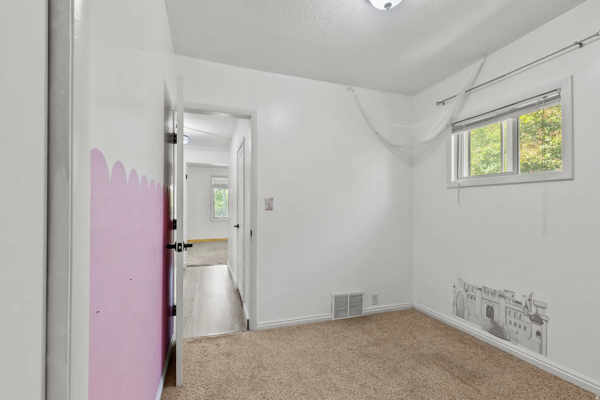 Carpeted room featuring a white ceiling, a single window with blinds, and a white wall with a decorative mural