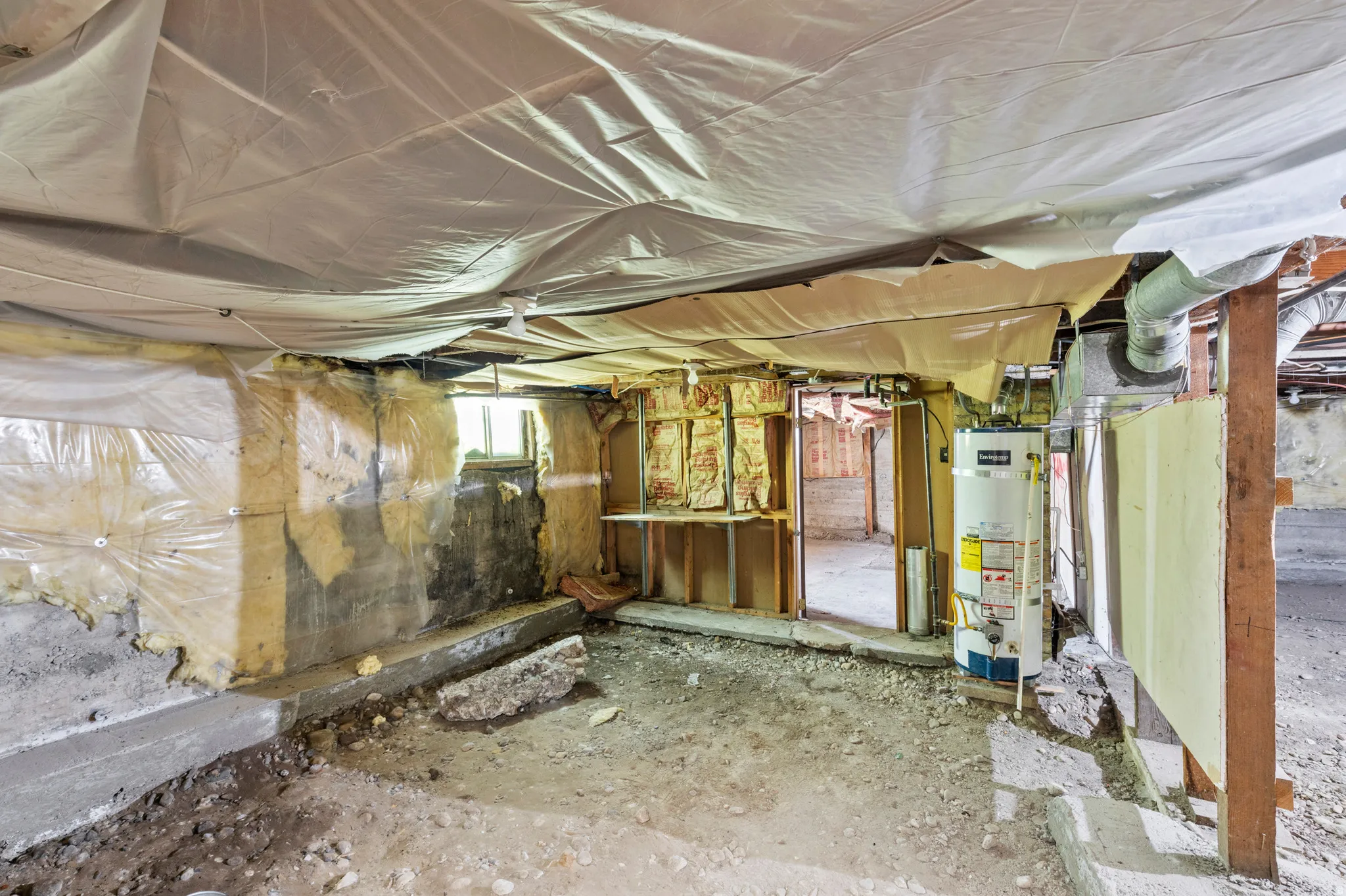 Unfinished basement space with exposed concrete walls, visible insulation, and structural framing