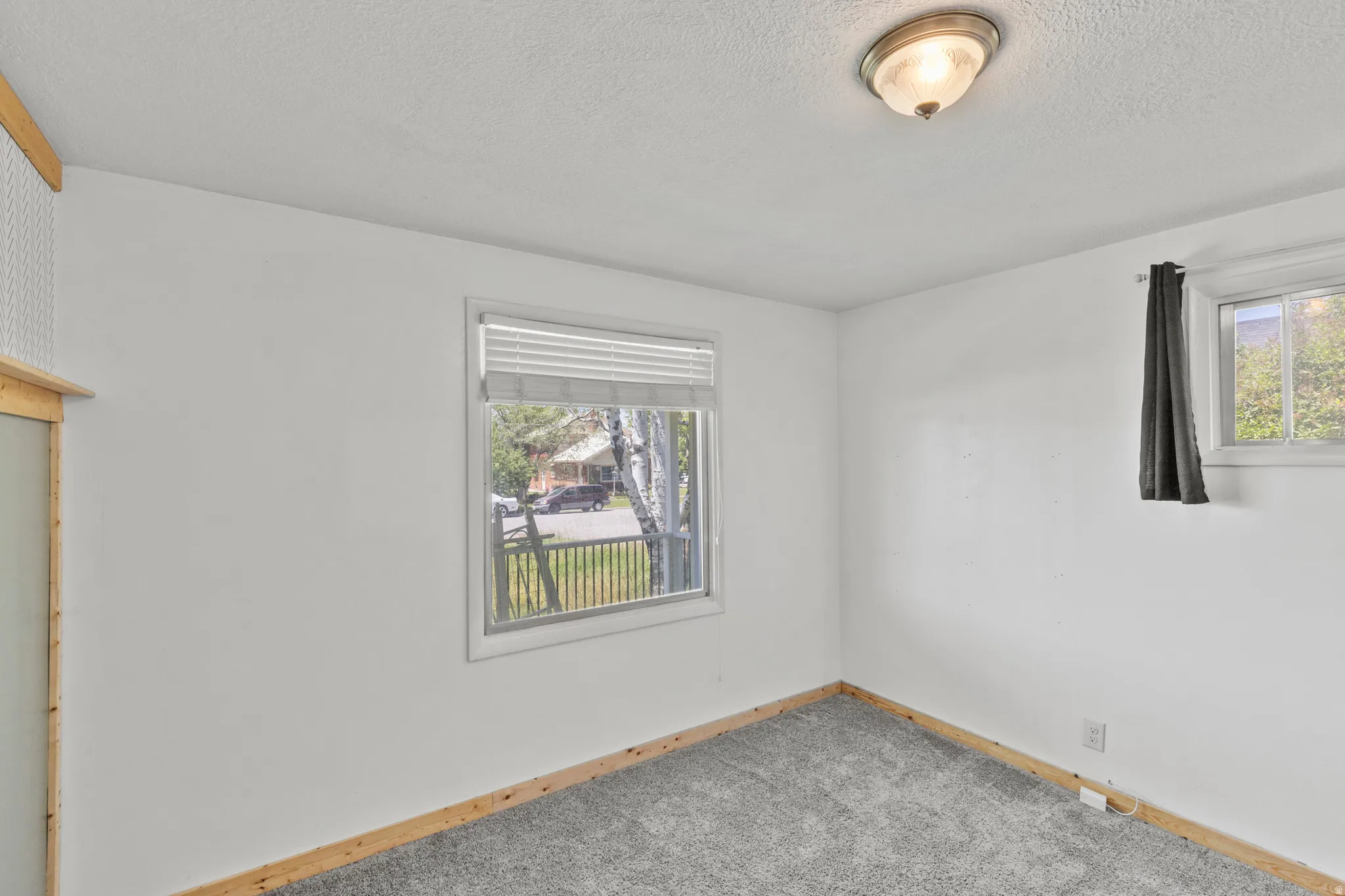 Room featuring two windows, neutral painted walls, and wood-finish baseboards. Hardwood is under the carpet.
