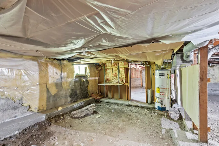 Unfinished basement space with exposed concrete walls, visible insulation, and structural framing