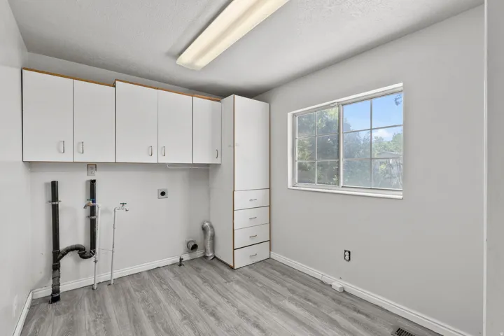 Laundry room featuring wood-finish flooring, overhead cabinetry, a built-in storage tower with drawers, and a large window. Closet with shelves also.  Gas and electric for dryer.  What great space; you could even have a craft room in here!