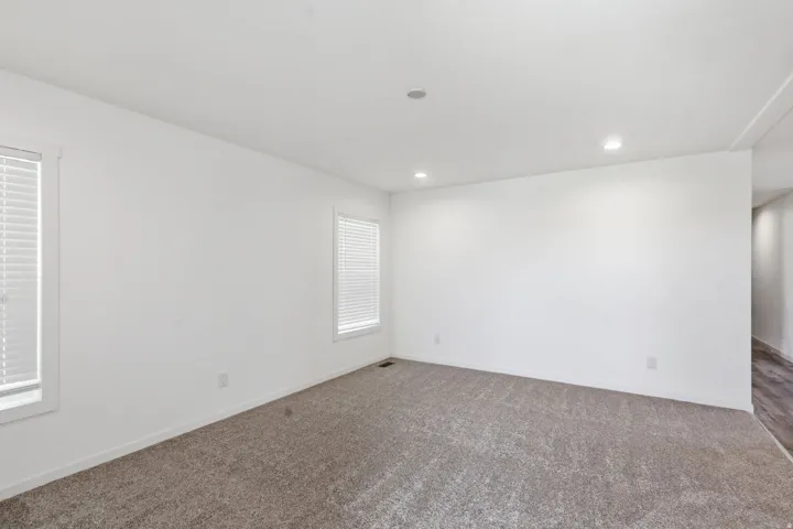 Spacious room featuring neutral carpeting, white walls, two windows with blinds, recessed lighting, and white trim