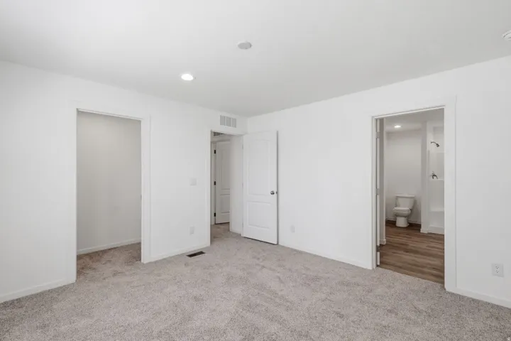 Neutral tone carpeted room featuring white walls, recessed lighting, and a white interior door
