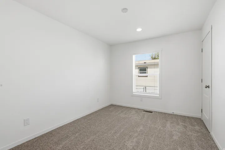 Bright room featuring neutral carpeting, a single window with blinds, recessed lighting, and a white interior door
