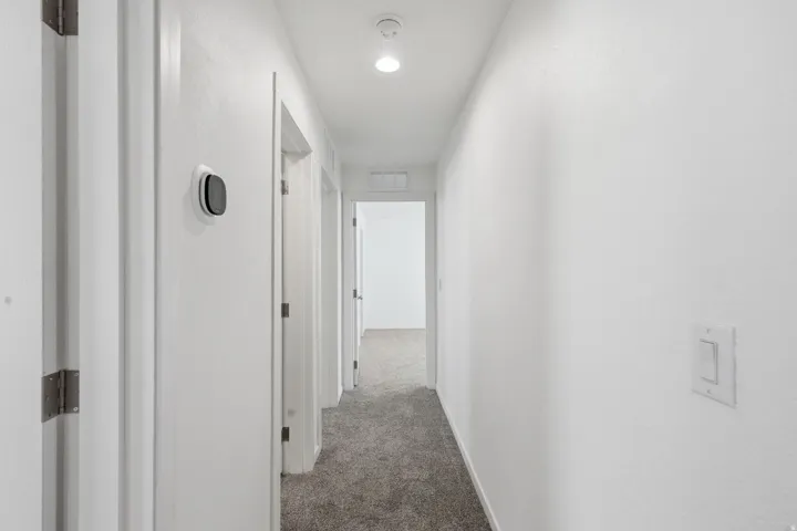 Hallway featuring light gray carpet, white walls, recessed lighting, and a modern thermostat