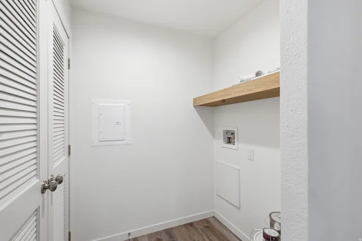 Utility area featuring wood-finish flooring, a floating wood-tone shelf, and white louvered bifold doors