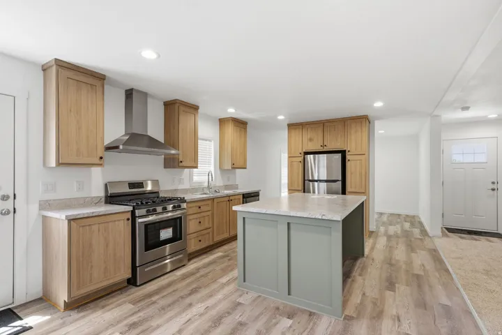 Kitchen featuring a central island with a light countertop, wood-finish flooring, stainless steel appliances, light wood cabinetry, and recessed lighting