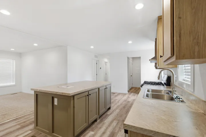 Kitchen featuring a central island with storage, light-toned countertops, a stainless steel sink with a gooseneck faucet, and wood-finish cabinetry