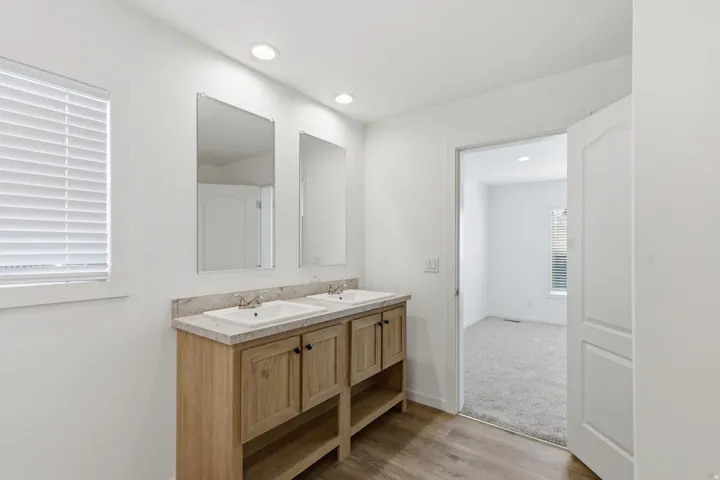 Dual vanity featuring light wood-finish cabinetry, white rectangular sinks, and a stone-look countertop
