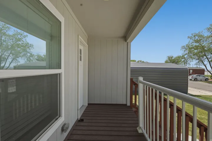 Covered porch entry featuring wood-look decking, white vertical siding, and a white railing with wood-tone balusters