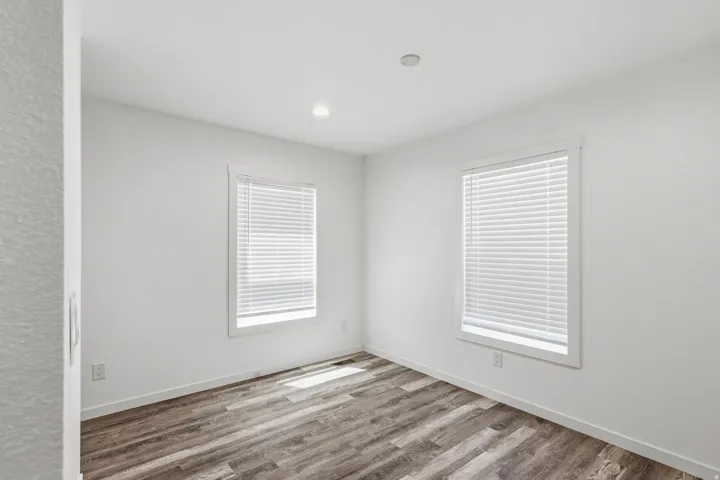 Room featuring two windows with white blinds, recessed lighting, and wood-finish flooring
