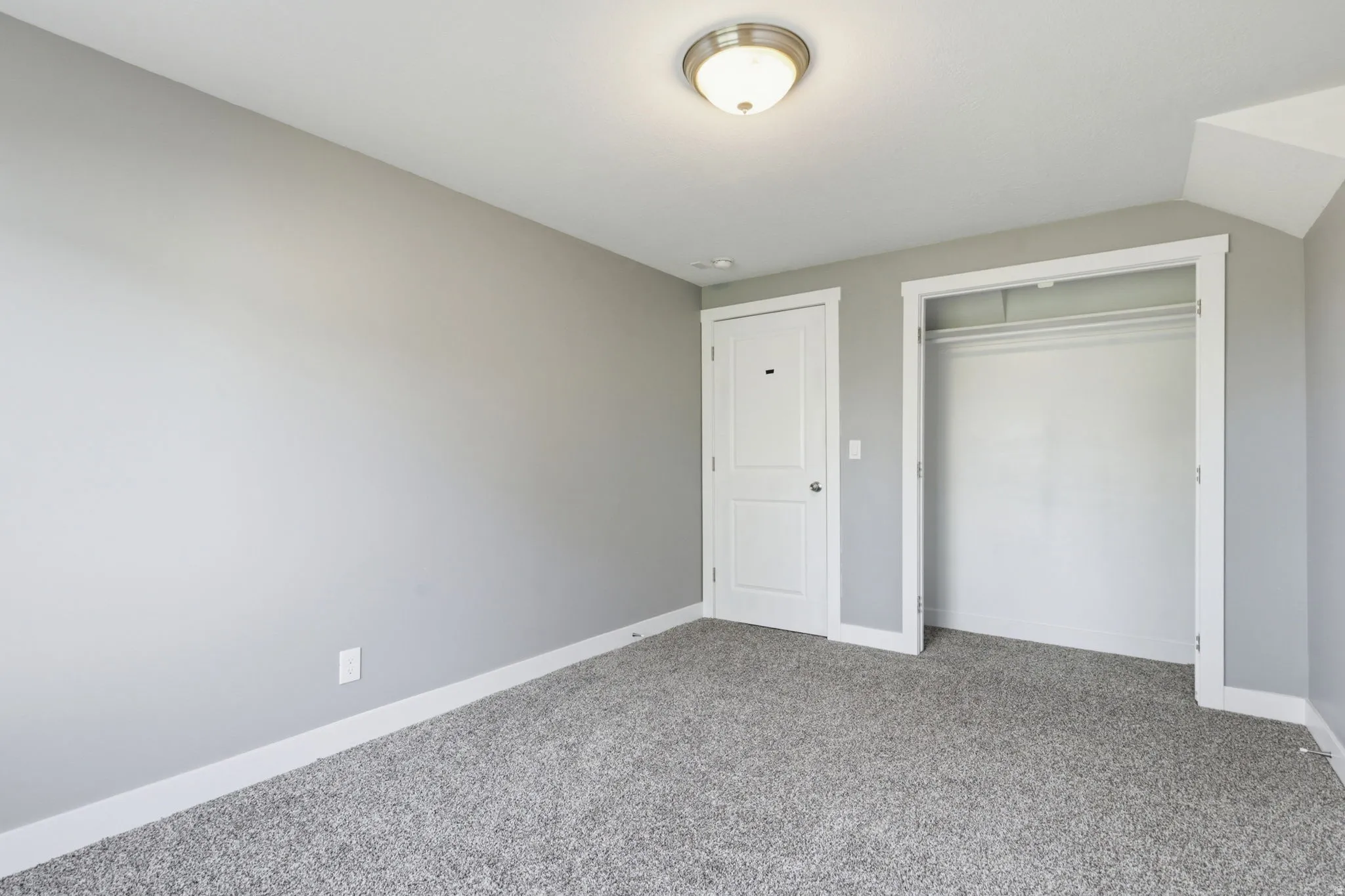 Neutral gray wall paint, textured gray carpeting, white baseboards, and a white interior door with a silver-tone handle