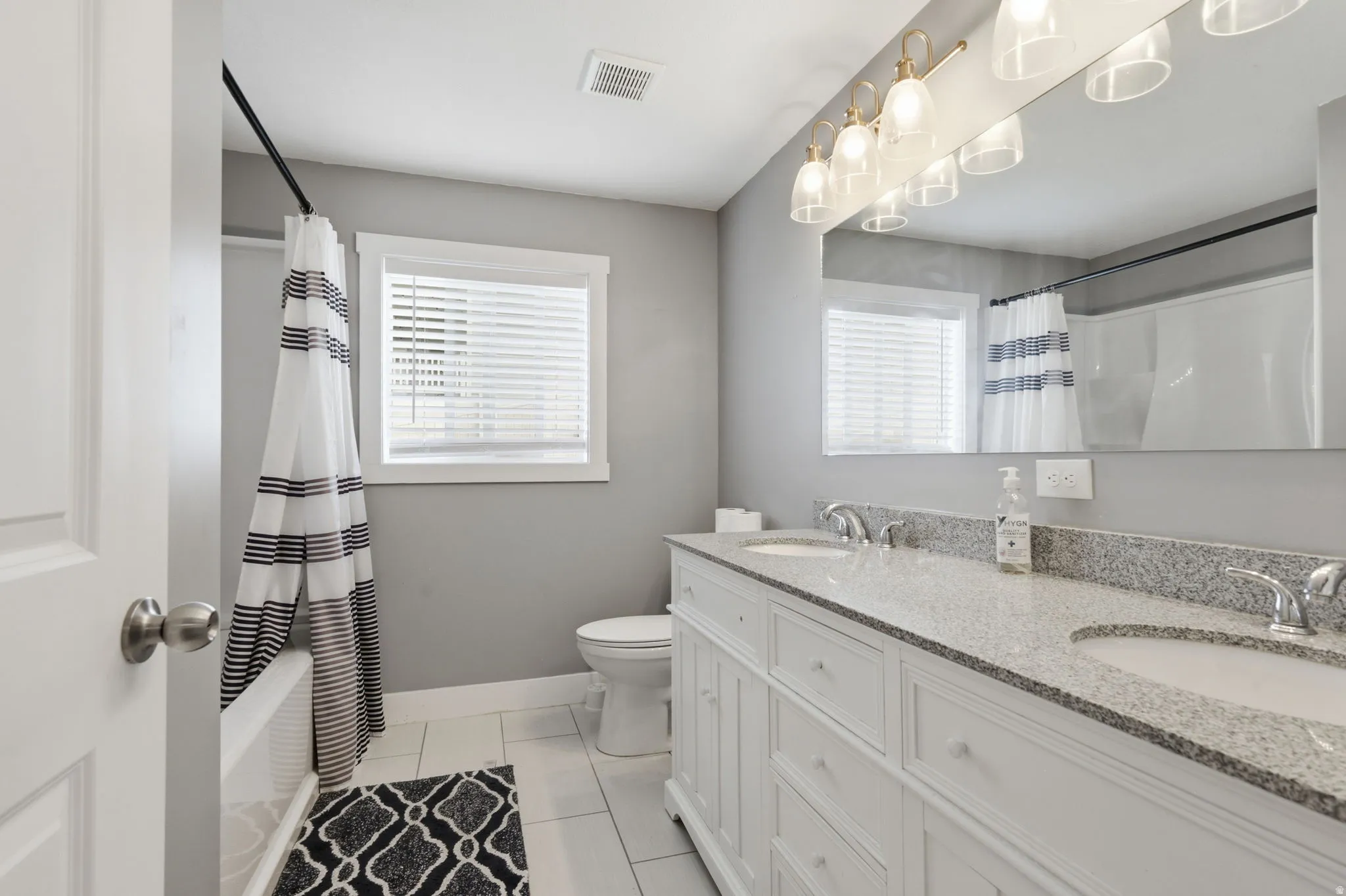 Dual vanity with granite countertops, chrome fixtures, and a large mirror