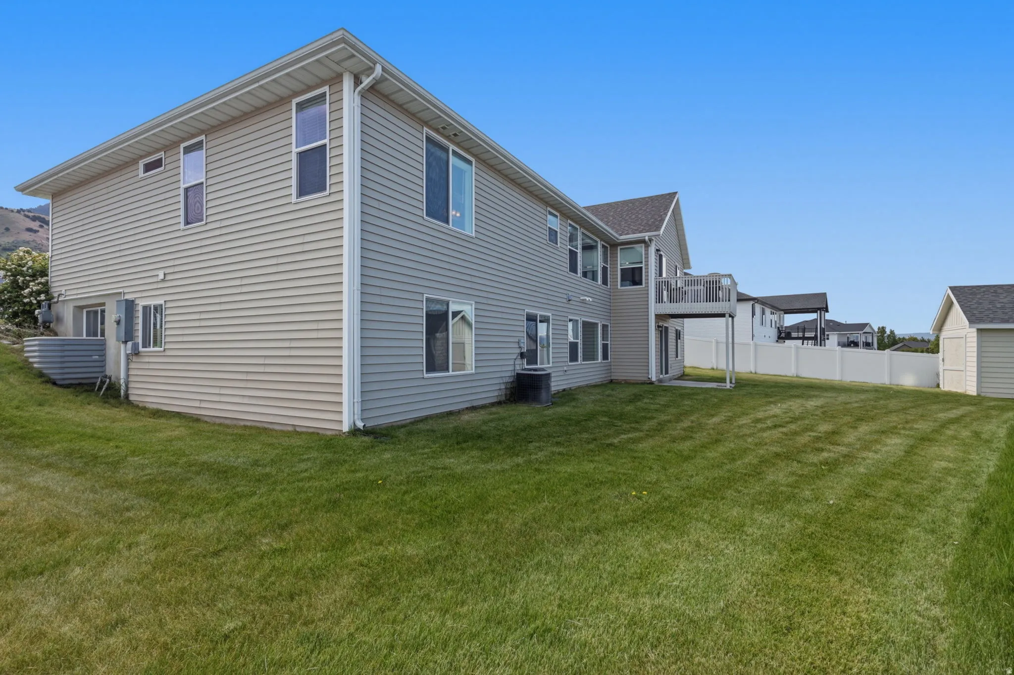 Expansive grassy backyard featuring a two-story home with light-colored siding, multiple windows, and a raised rear deck