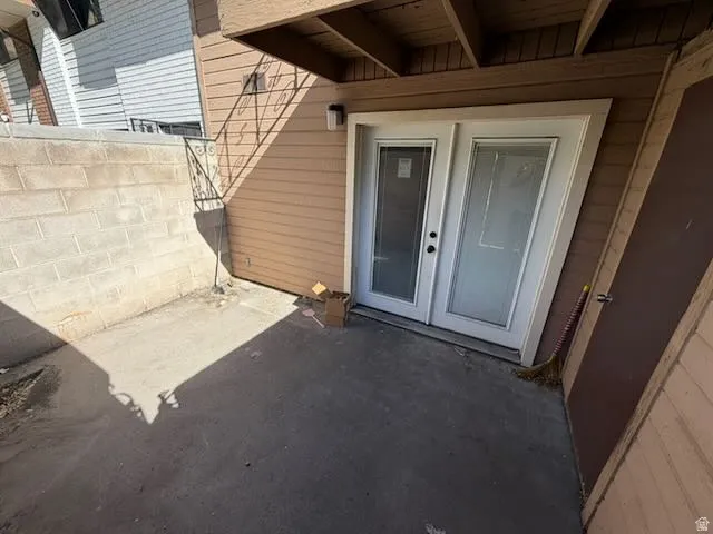 Private concrete patio featuring double-pane glass doors with black hardware, a built-in exterior storage closet, and a concrete block retaining wall