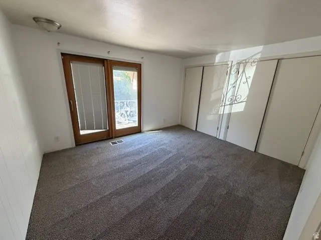Spacious room featuring wood-framed glass sliding doors, dark gray carpet, two sliding closet doors, a white paneled wall, and a flush-mount ceiling light fixture