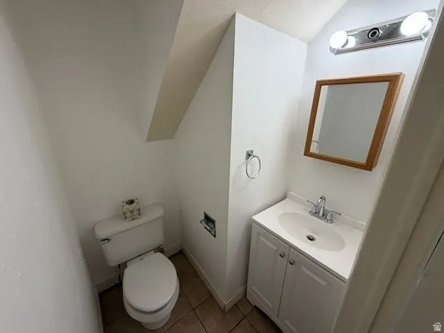 Compact bathroom featuring a white toilet, floor-mounted vanity with a single sink, wood-framed mirror, and overhead vanity lighting