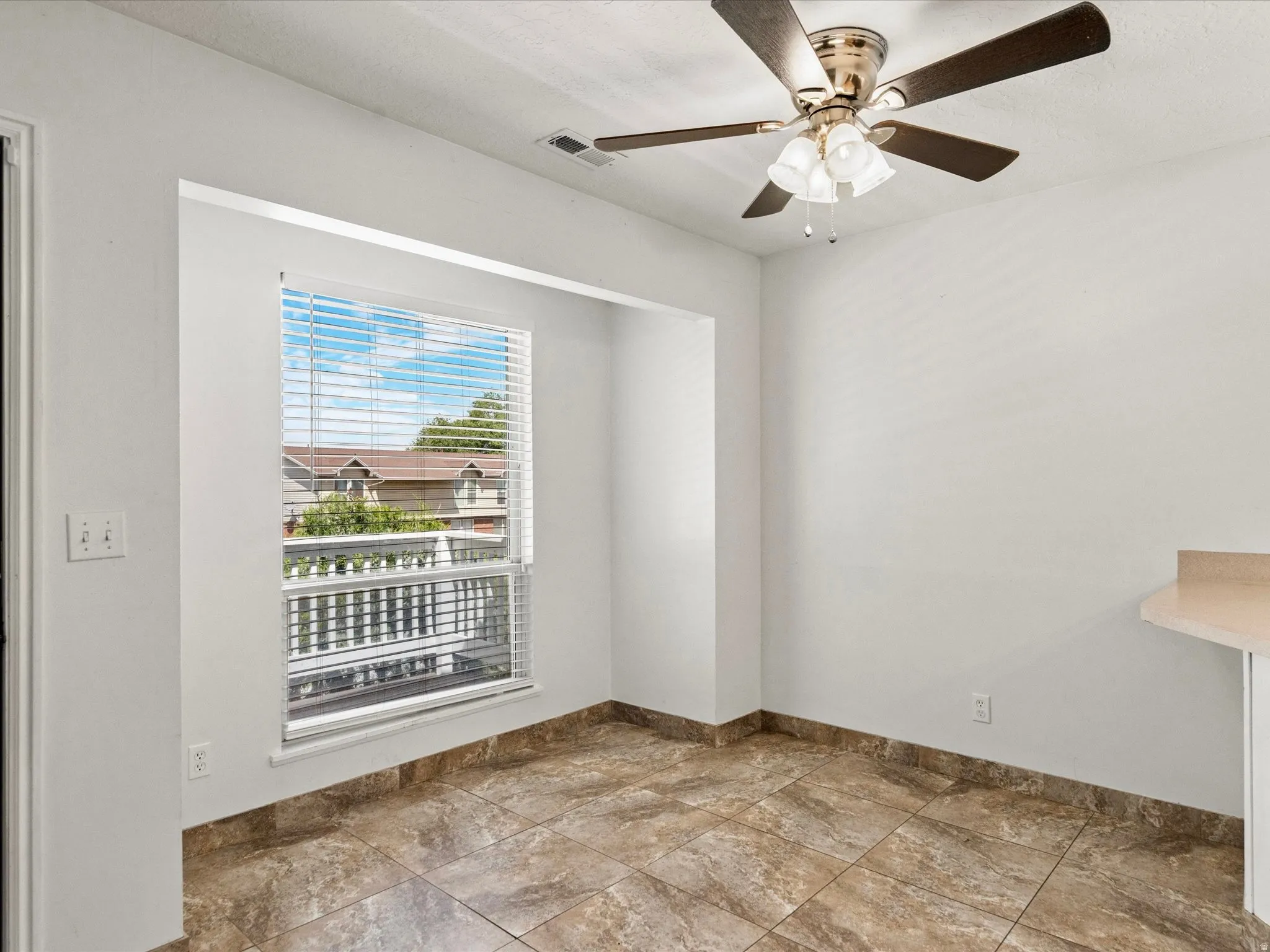 Bright interior space featuring a window with horizontal blinds, ceiling fan with integrated lighting, and ceramic tile flooring