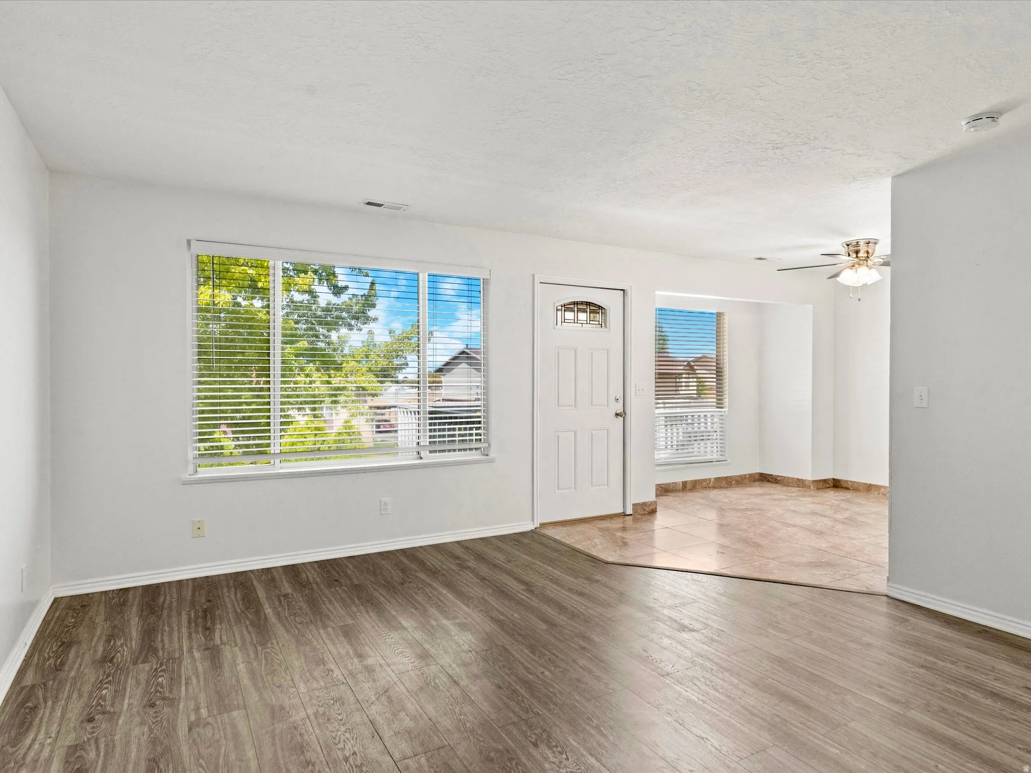 Entry room featuring wood-finish flooring, a white front door with an arched window insert, and a large window with blinds