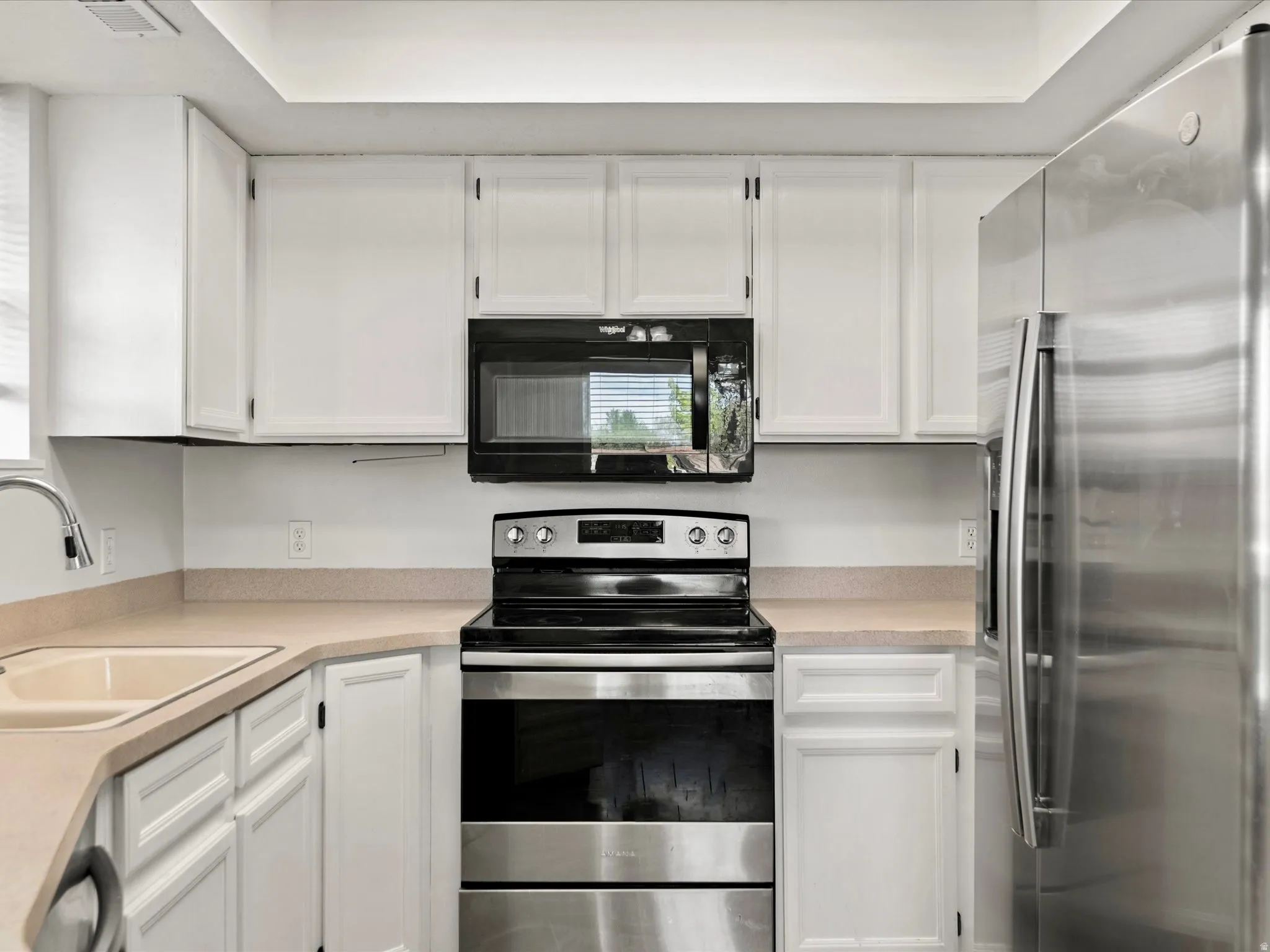 Kitchen featuring white cabinetry, light-toned countertops, stainless steel appliances, a corner sink with a gooseneck faucet, and an overhead microwave