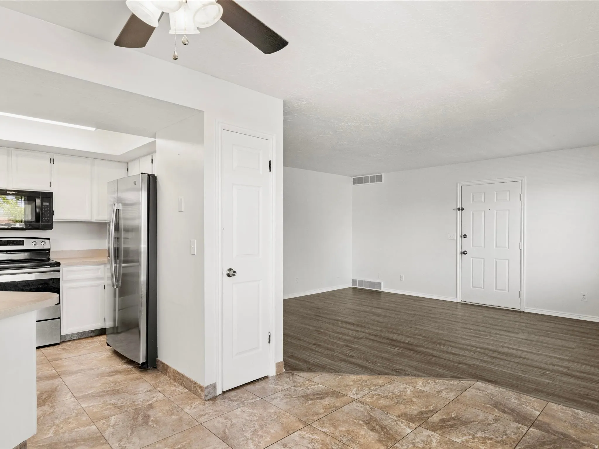 Kitchen and living area featuring a ceiling fan, wood-finish flooring, white paneled doors, and stainless steel appliances