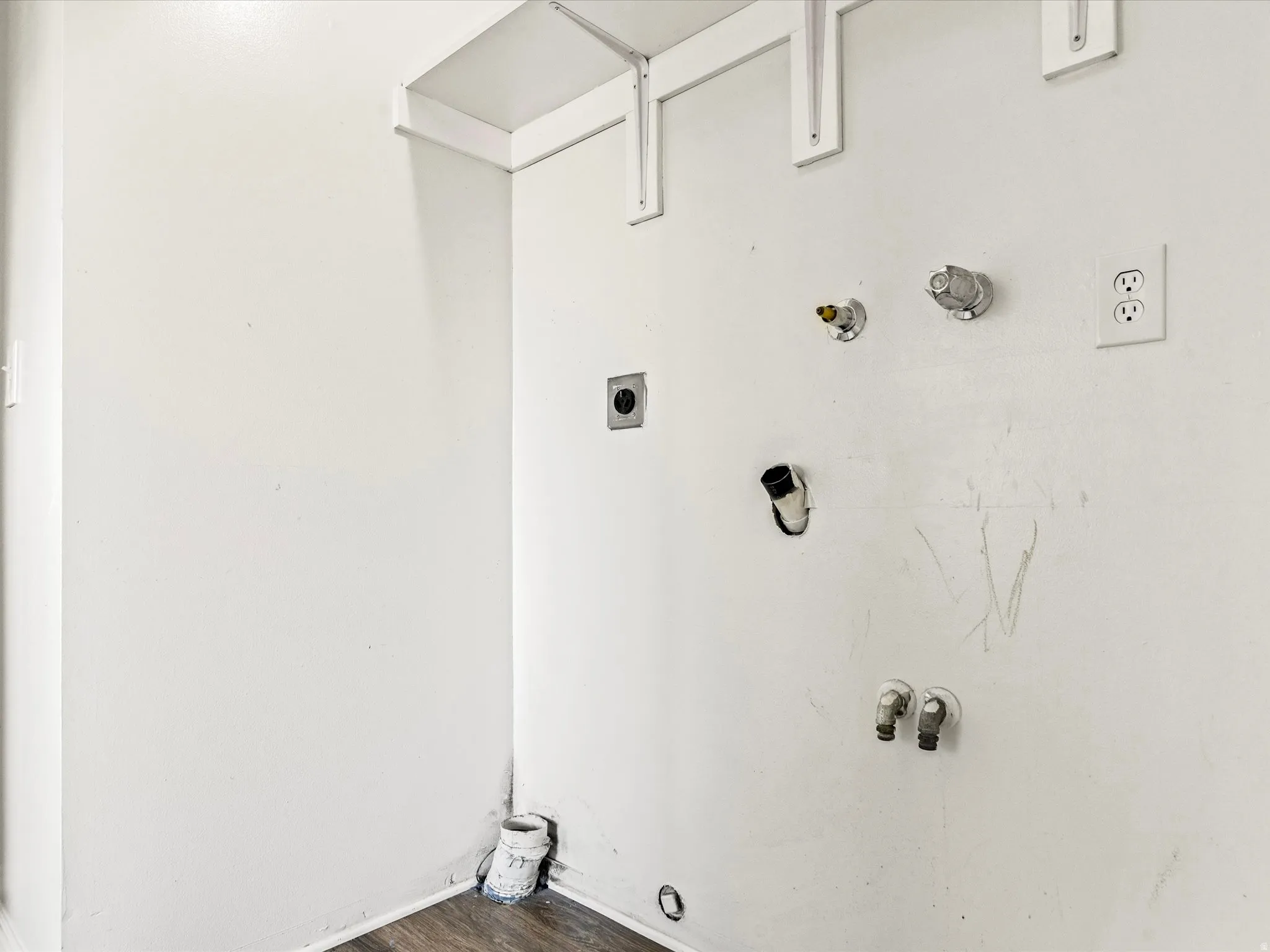 Dedicated laundry area featuring white walls, wood-finish flooring, and plumbing connections for appliances