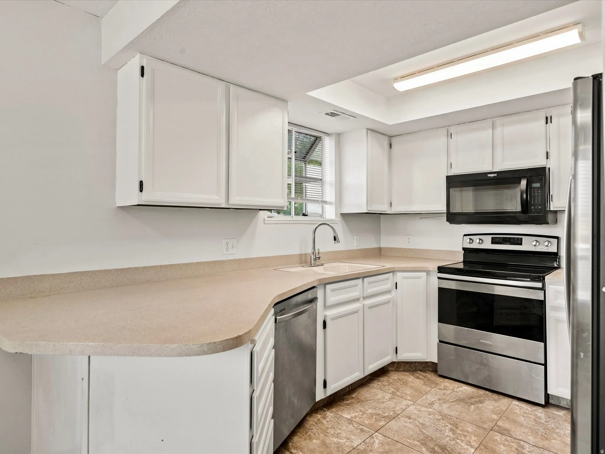 Kitchen featuring white cabinetry, light-toned countertops, a stainless steel dishwasher, a stainless steel range with a black microwave above, and tiled flooring