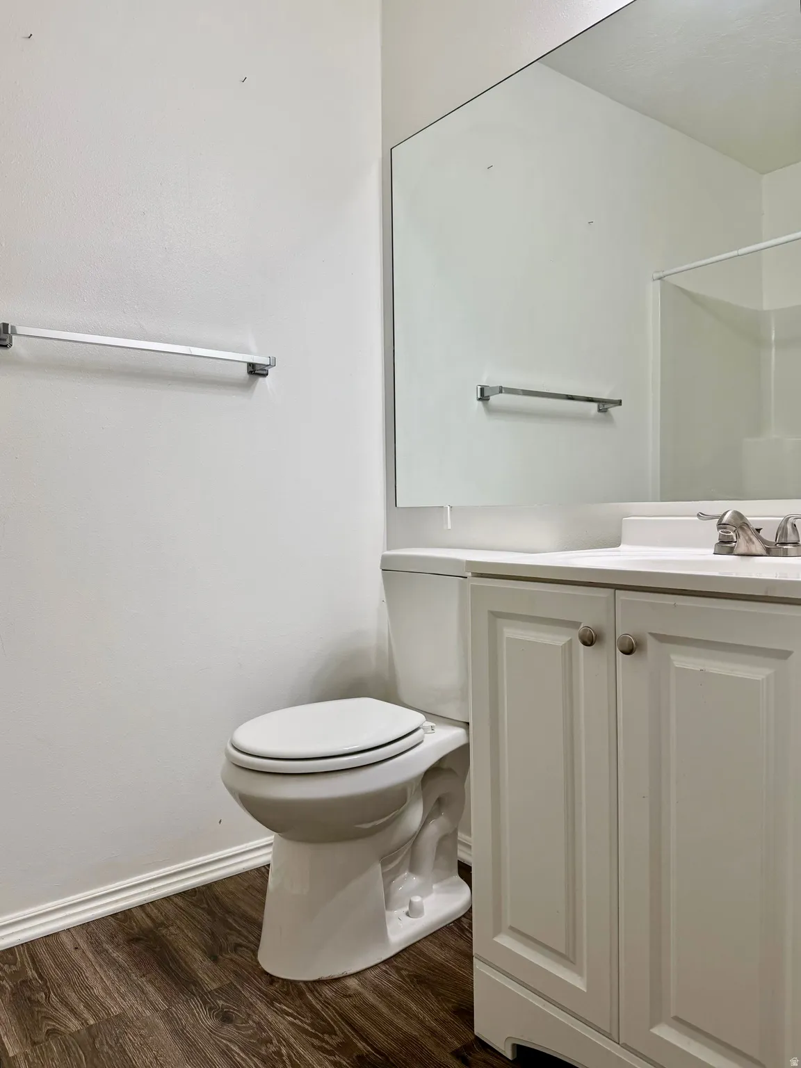 Bathroom featuring wood-finish flooring, a white vanity with paneled doors, a white countertop, a white toilet, and a large wall-mounted mirror