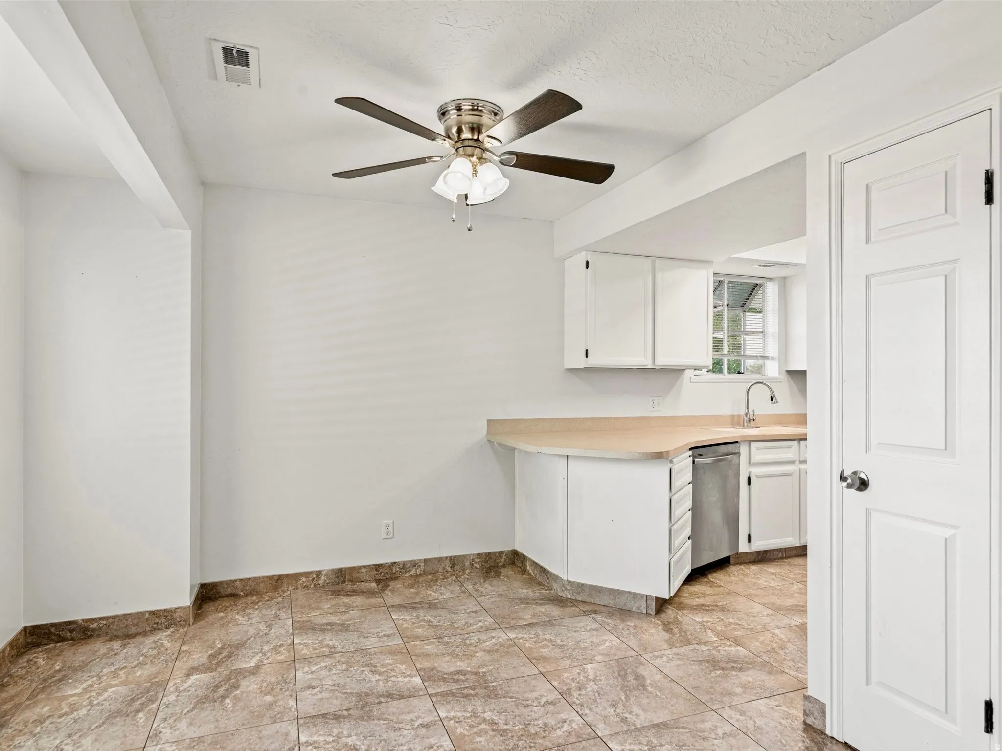 Kitchen area featuring a stainless steel dishwasher, white cabinetry, and a light-toned countertop